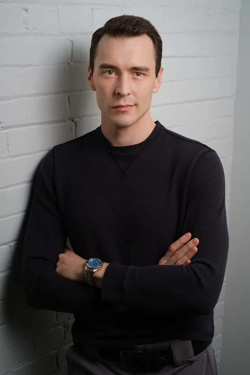 Actor portrait of a man with arms crossed against a white brick wall