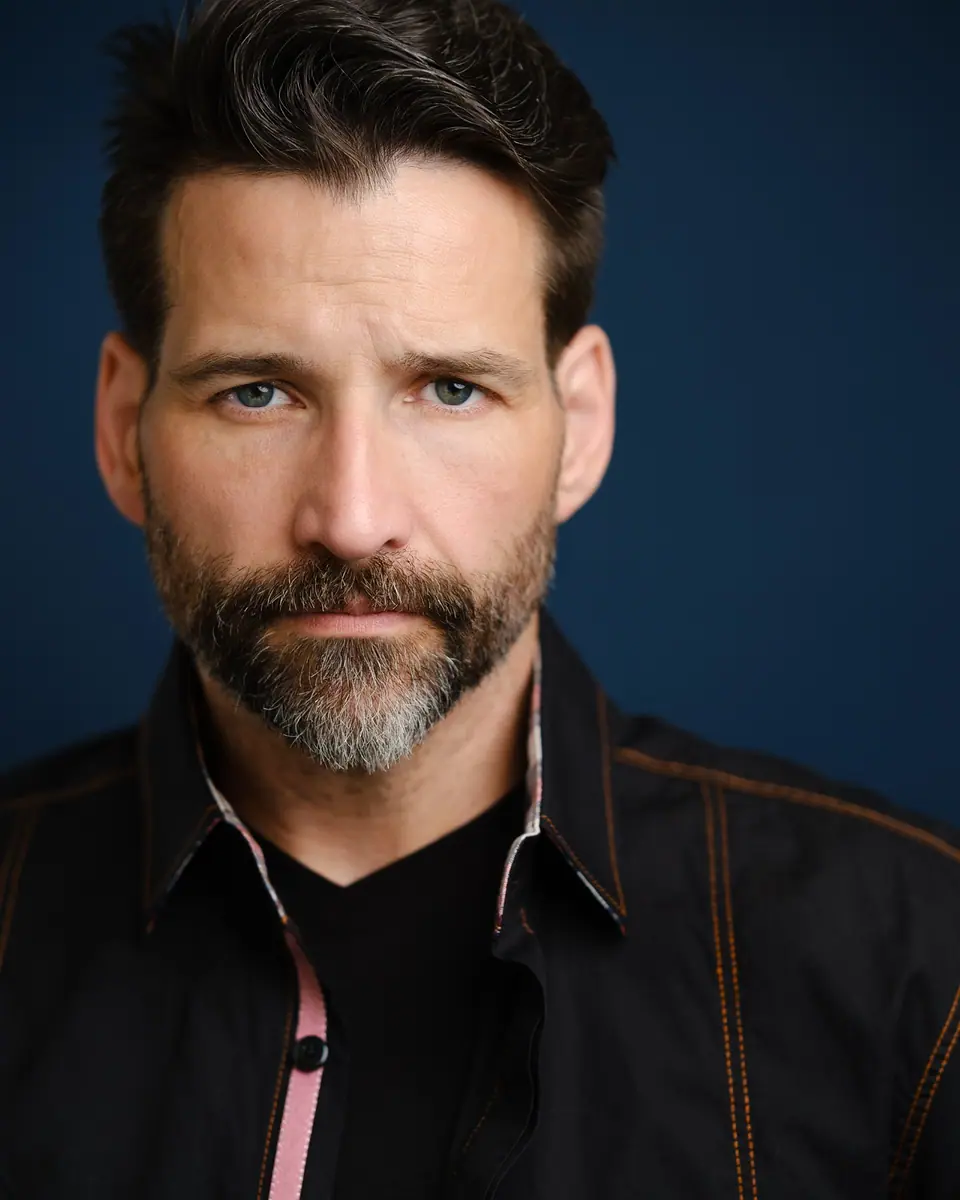Moody actor headshot of a bearded man on a deep blue backdrop