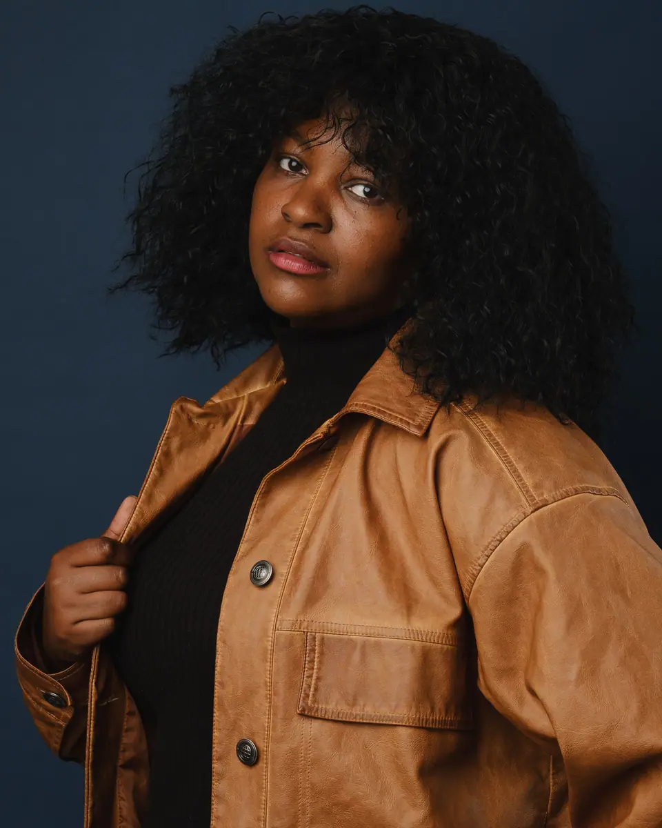 Actor headshot of a woman with natural curls in a tan leather jacket