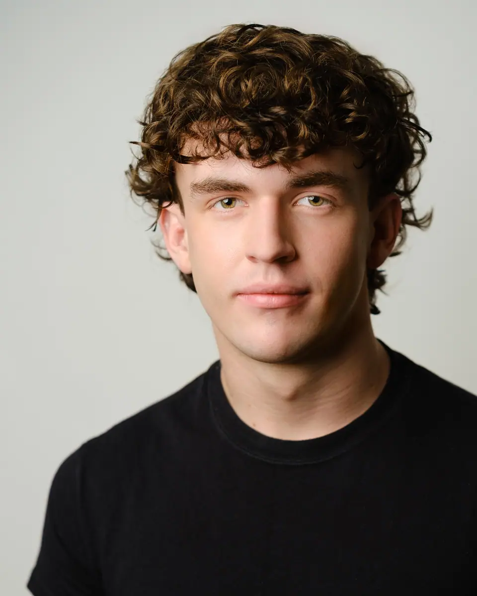 Actor headshot of a young man with curly hair in a black tee