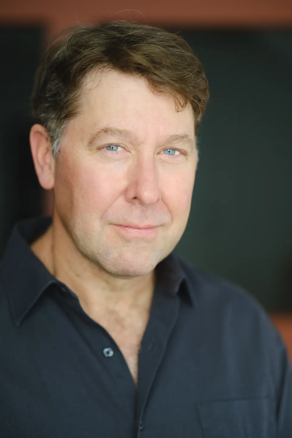 Actor headshot of a man in a dark shirt with warm background light