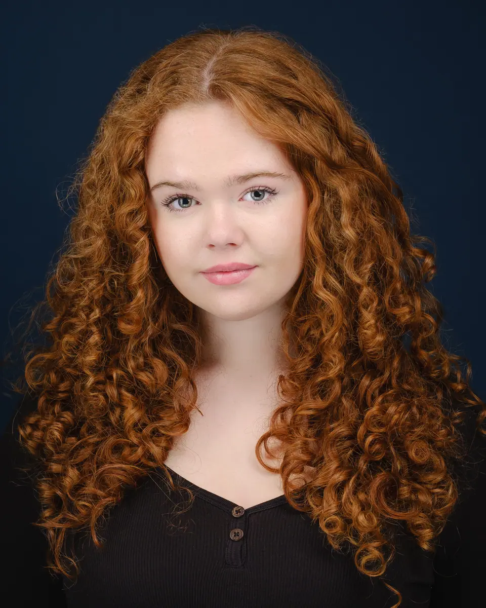 Actor headshot of a young woman with long red curls on a navy backdrop