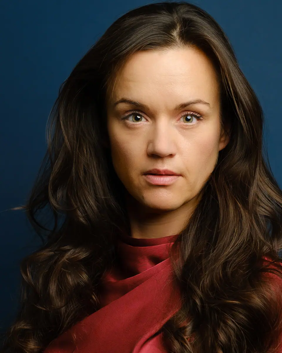 Theatrical actor headshot of a woman with long dark hair on a teal blue backdrop