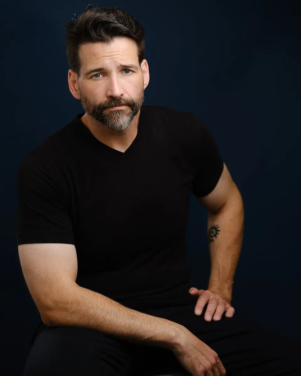 Actor portrait of a man in a black t shirt seated on a dark set