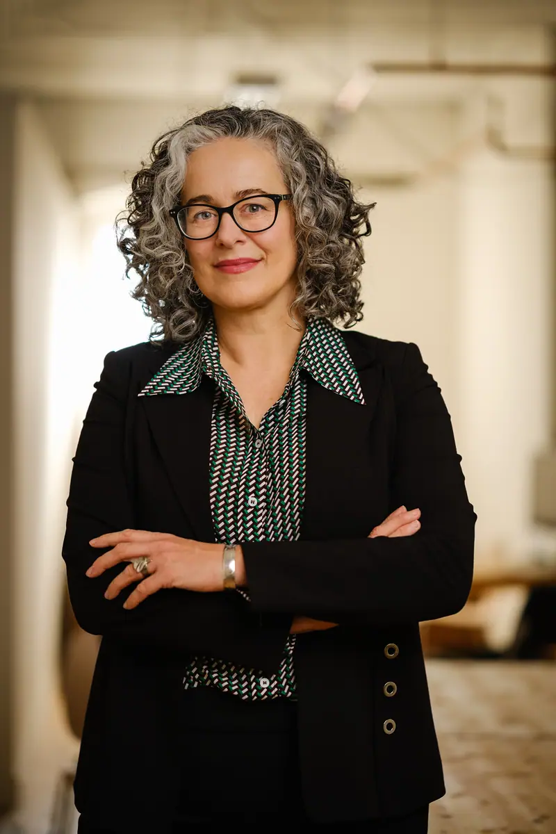 Personal branding portrait of a woman with curly grey hair and glasses, arms crossed