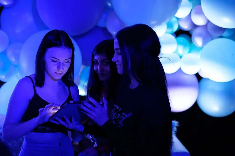 Guests checking photos on their phones in front of a glowing balloon installation