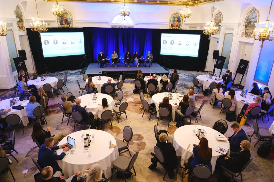 Wide shot of a conference ballroom with round tables and stage screens