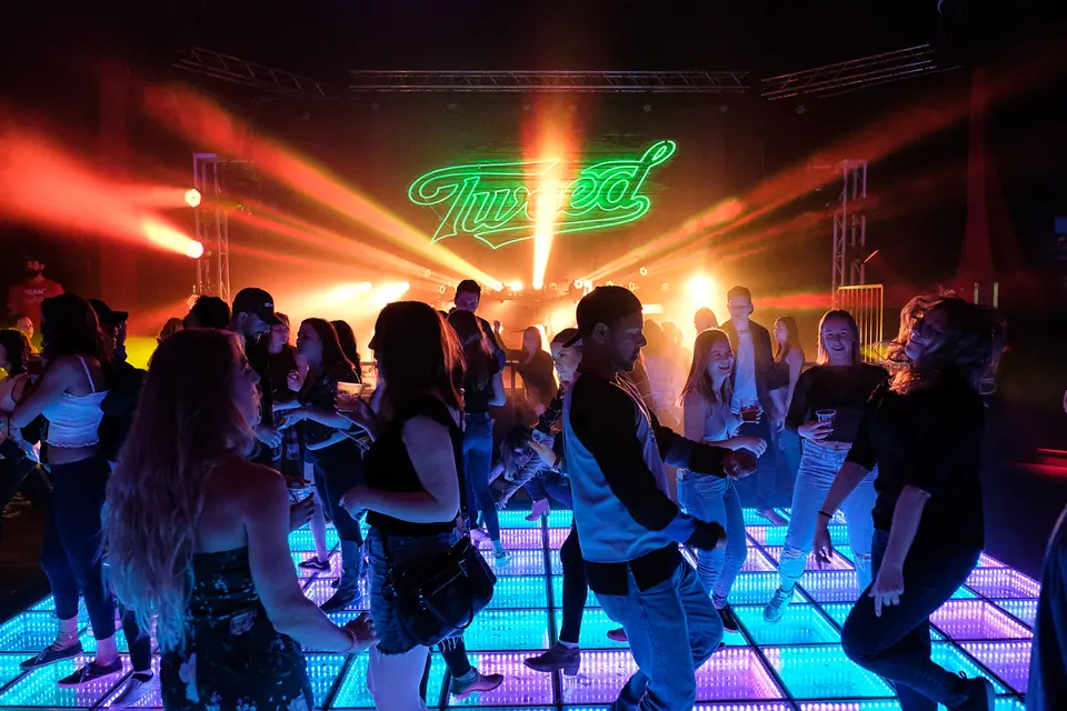 Corporate party with guests on a lit dance floor under a neon sign