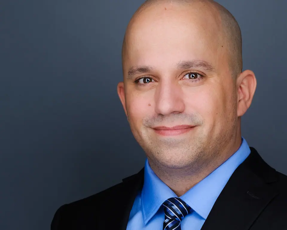 Corporate headshot of a bald man in a dark suit and blue tie