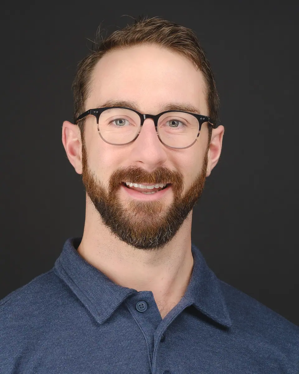 Headshot of a smiling man with glasses and a beard in a blue polo