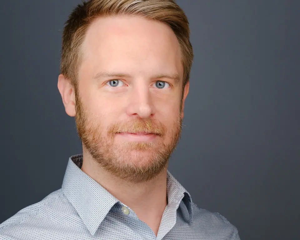 Relaxed headshot of a man with a short red beard in a light grey shirt