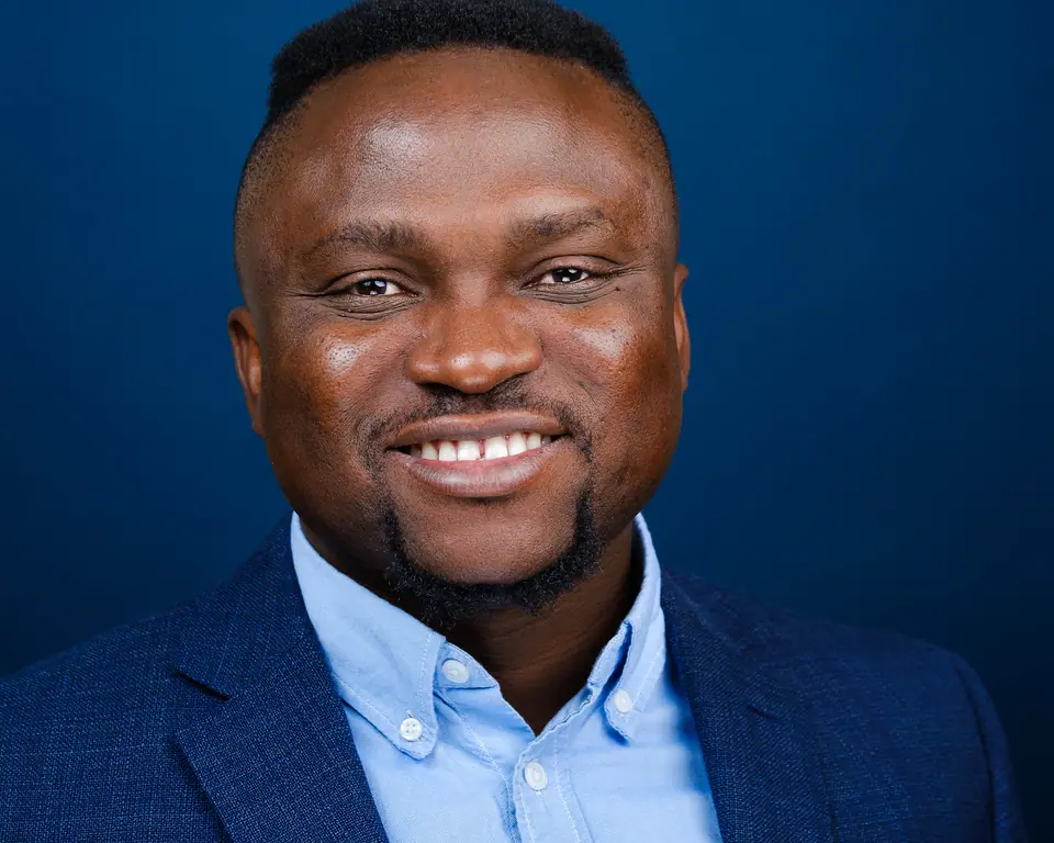 Bright headshot of a smiling man in a navy blazer on a deep blue backdrop