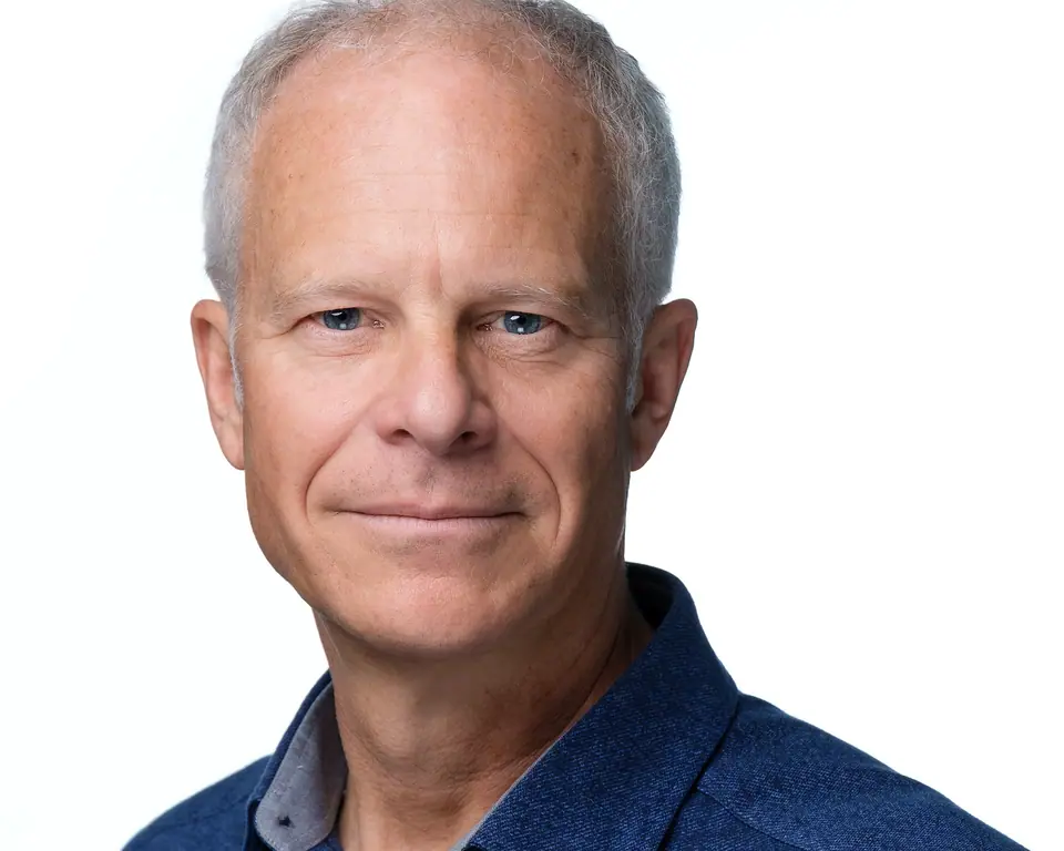Headshot of a man with grey hair in a blue jacket on white