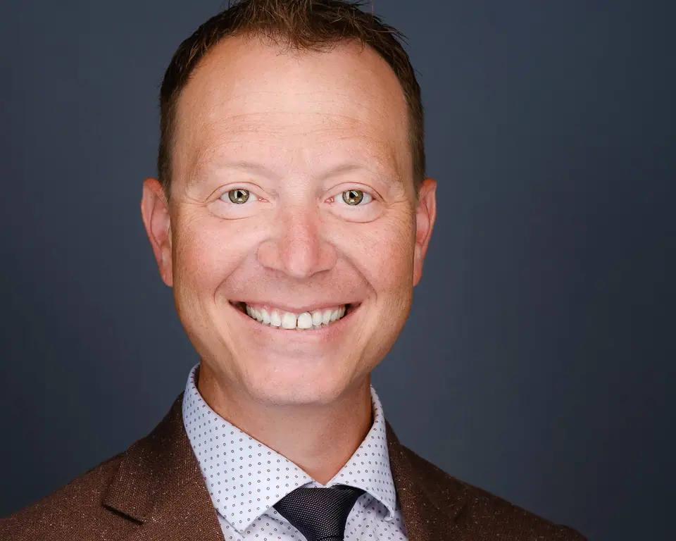Headshot of a laughing man in a brown jacket and dark tie