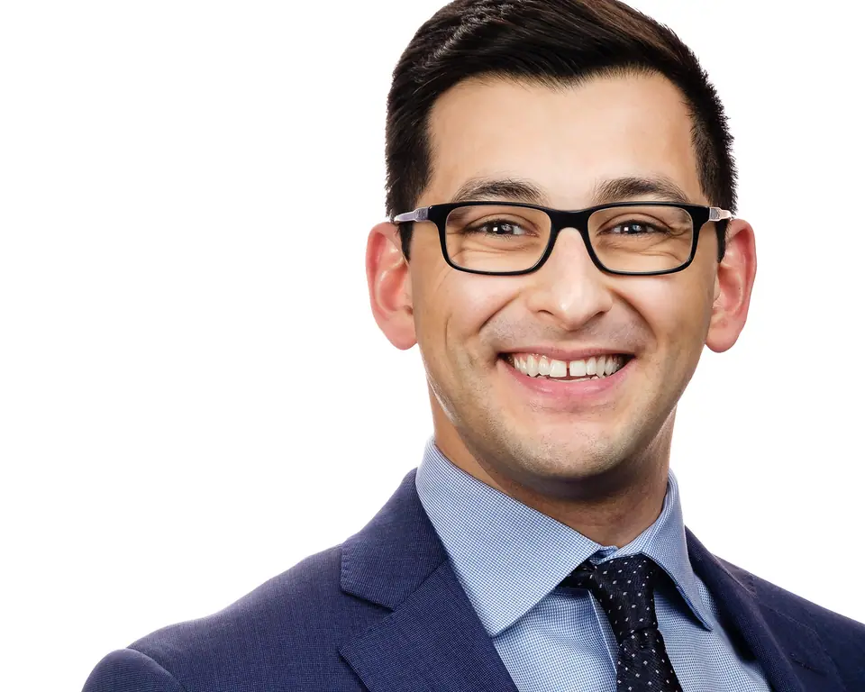 Headshot of a smiling man with glasses in a navy suit