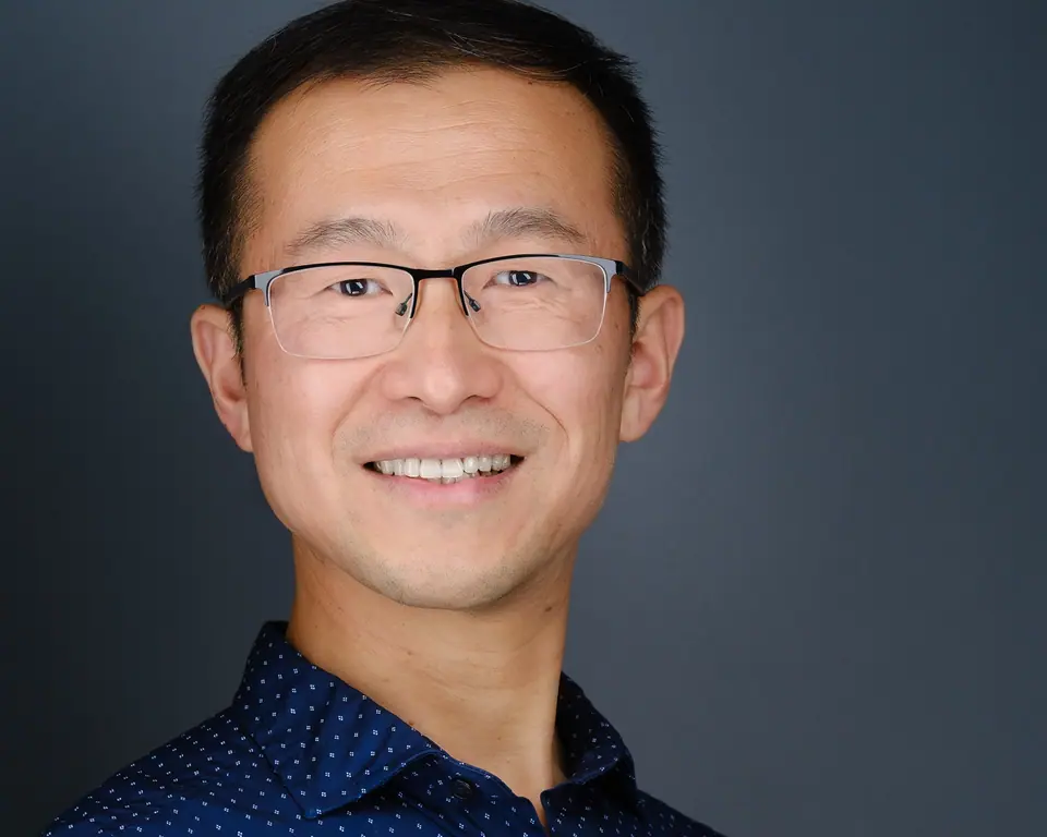 Headshot of a smiling man with glasses in a dark patterned shirt
