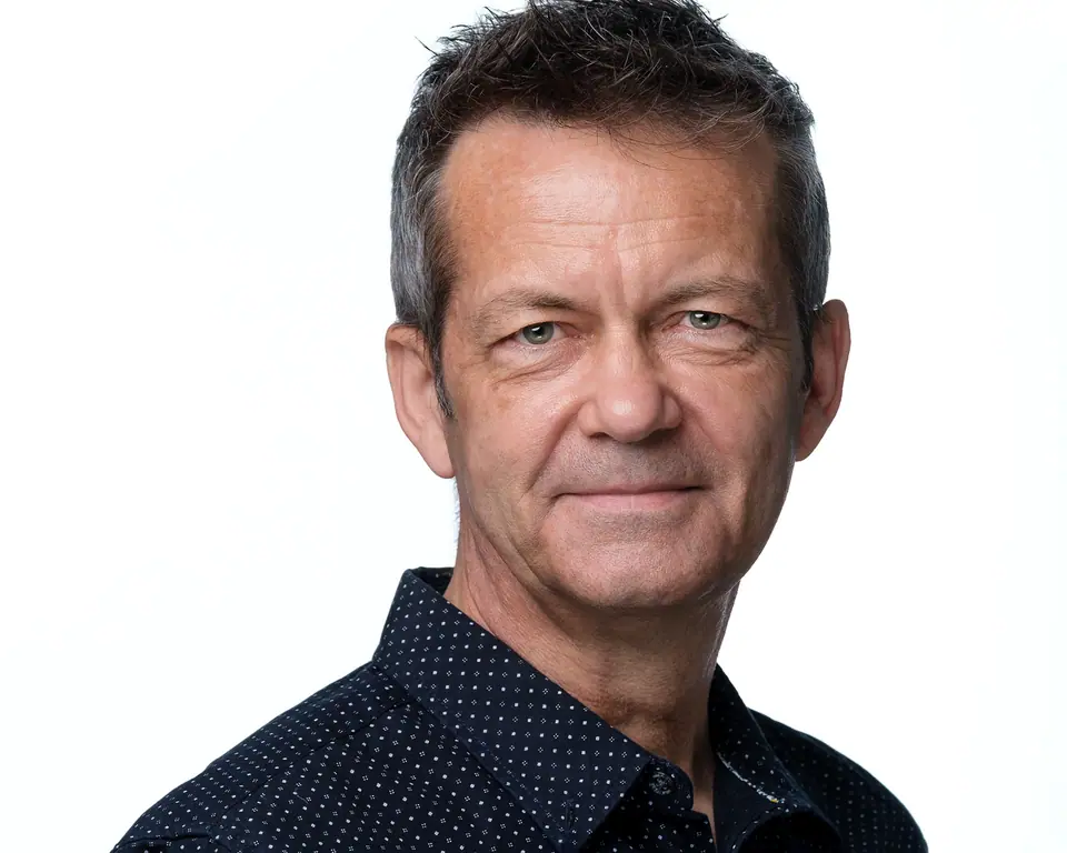 Light background headshot of a man with grey hair in a dark shirt