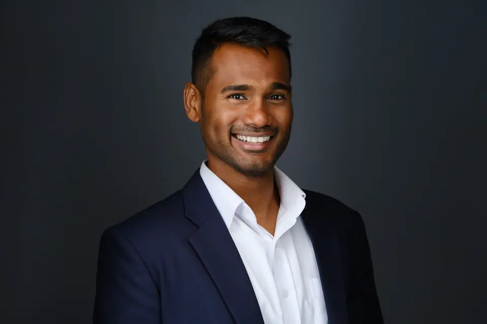 Business headshot of a smiling man in a navy blazer and white shirt