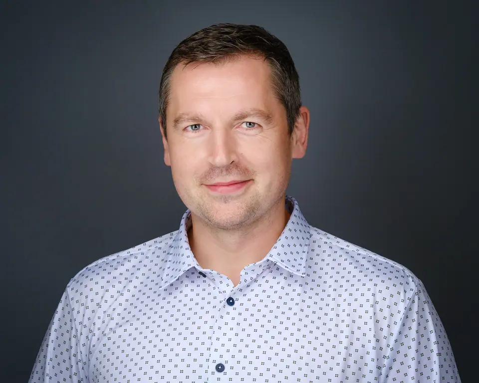 Headshot of a man in a patterned shirt on a grey backdrop