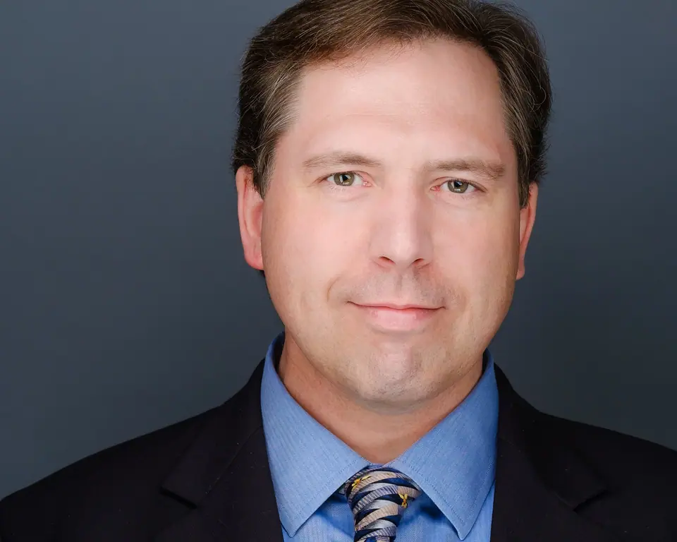 Business headshot of a man in a suit, blue shirt and striped tie