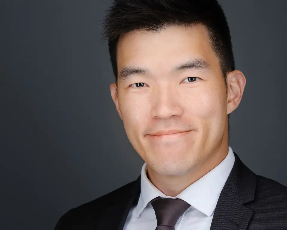Corporate headshot of a man in a dark suit and tie on grey