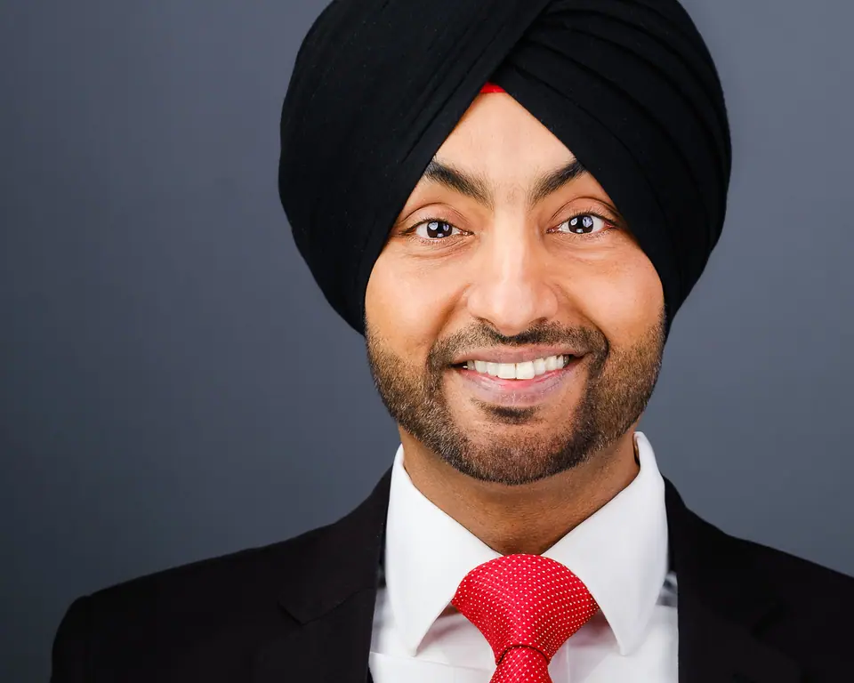 Professional headshot of a smiling man wearing a black turban and red tie