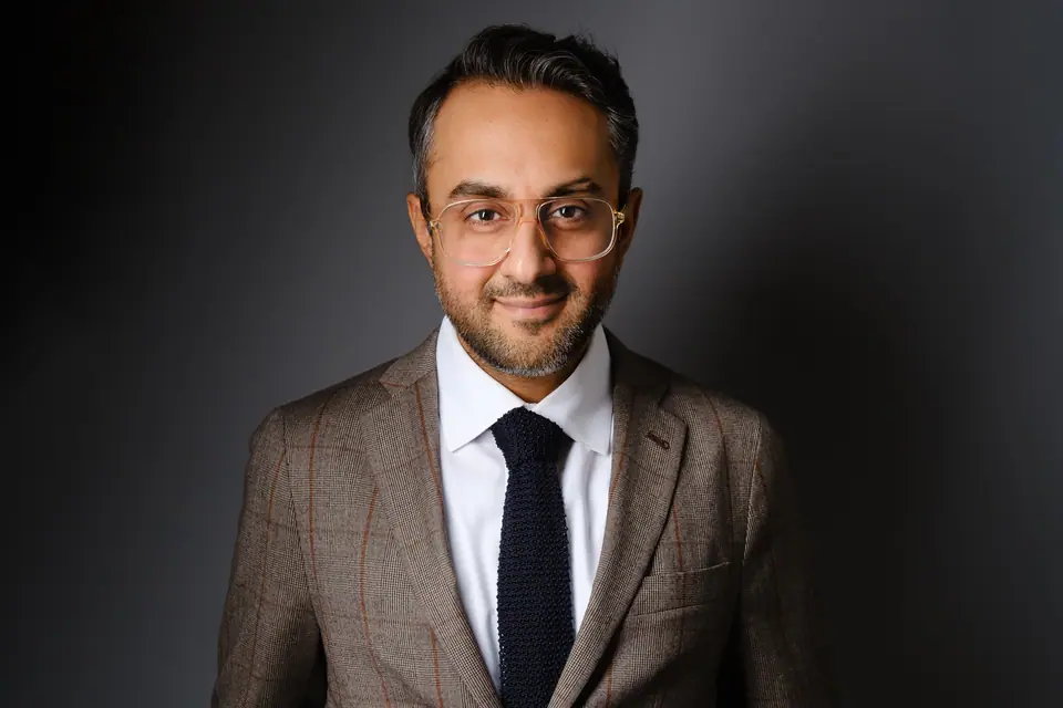 Executive headshot of a man with glasses in a tweed jacket and navy tie