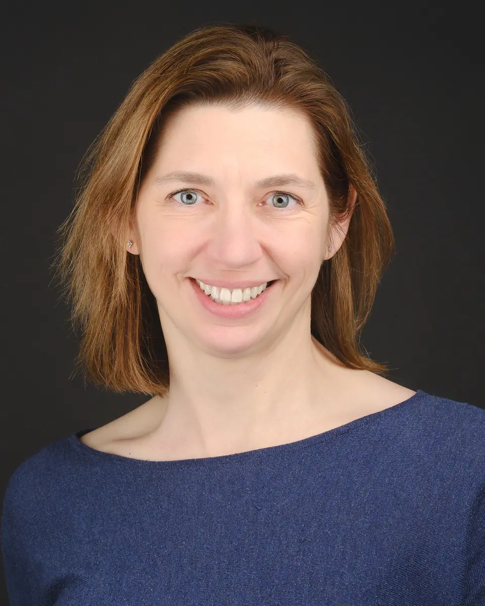 Headshot of a smiling woman with auburn hair in a navy top