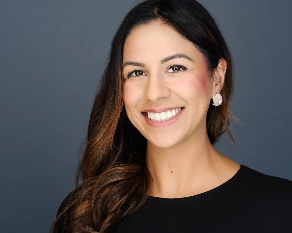 Studio headshot of a smiling woman with long dark hair on a grey backdrop