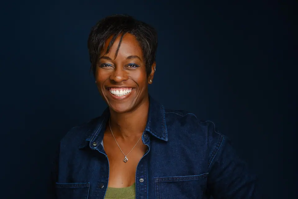 Headshot of a smiling woman in a denim jacket on a navy backdrop