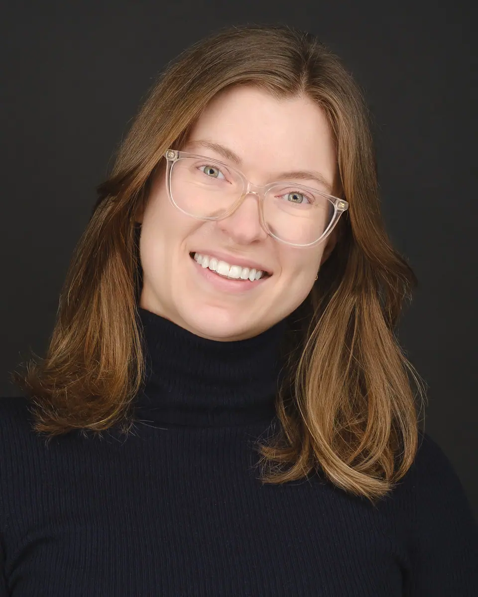 Headshot of a smiling woman with glasses in a black turtleneck