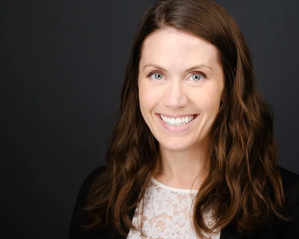 Headshot of a smiling woman with long brown hair on a dark backdrop