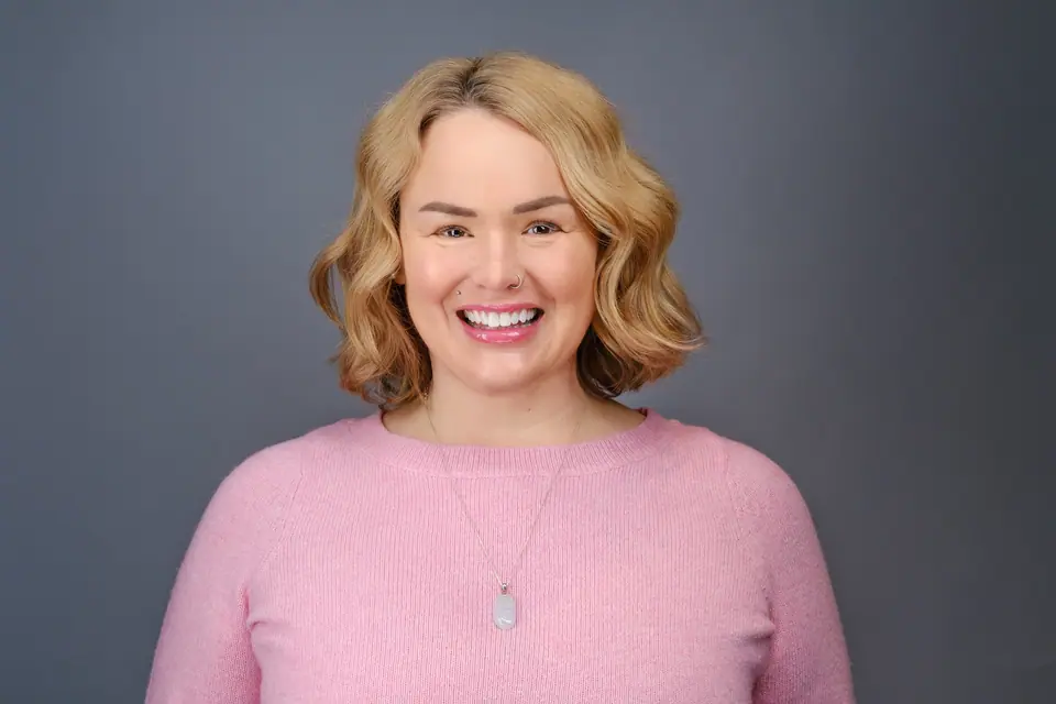 Bright headshot of a laughing woman with curly blonde hair in a pink sweater