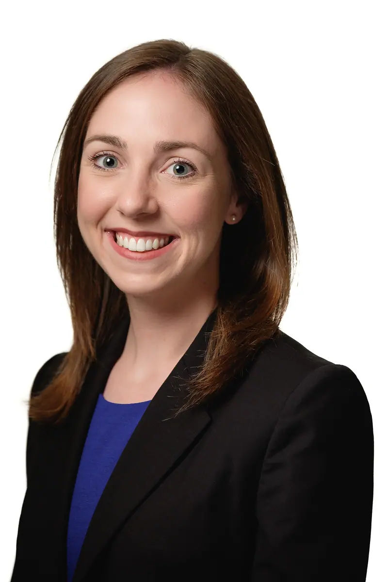Professional headshot of a smiling woman in a black blazer on white