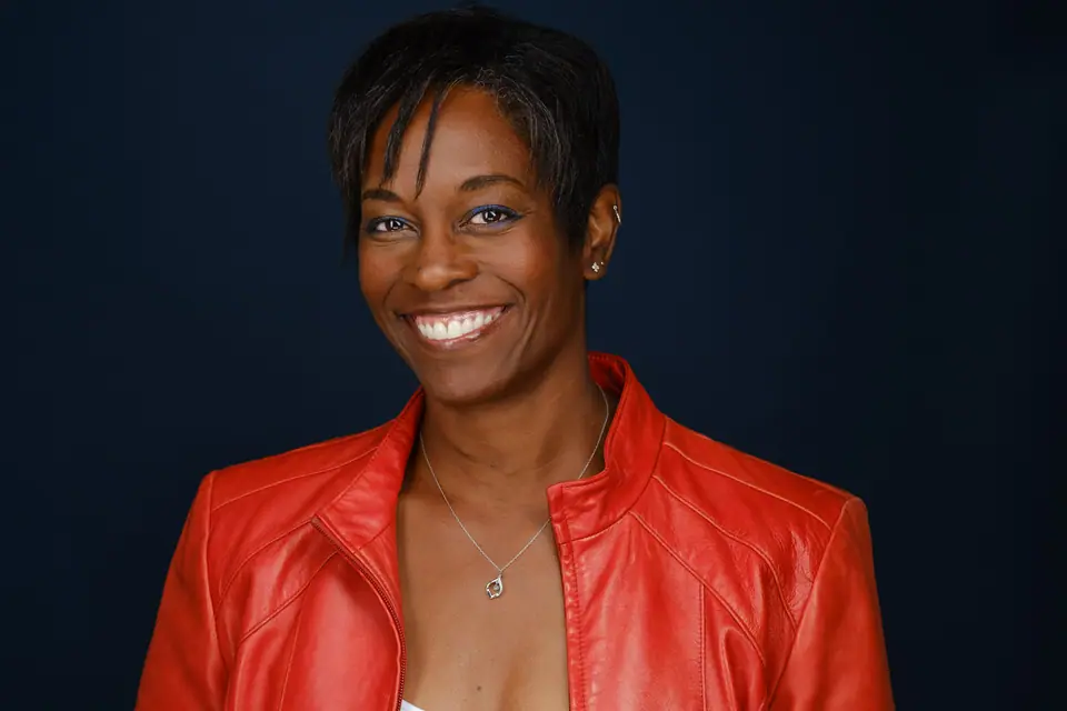 Bold headshot of a smiling woman in a red leather jacket on a dark backdrop