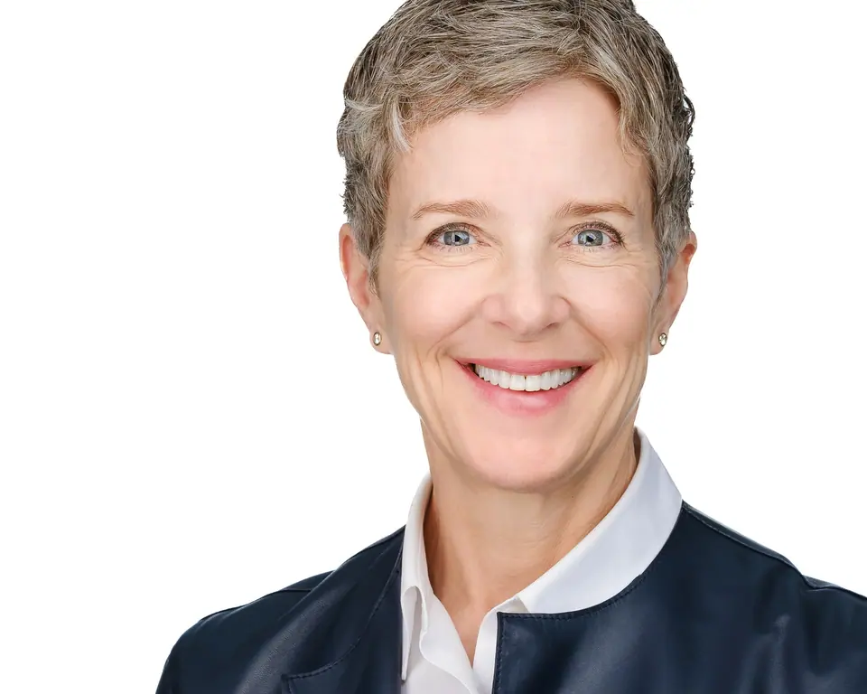 White background headshot of a smiling woman with short grey hair