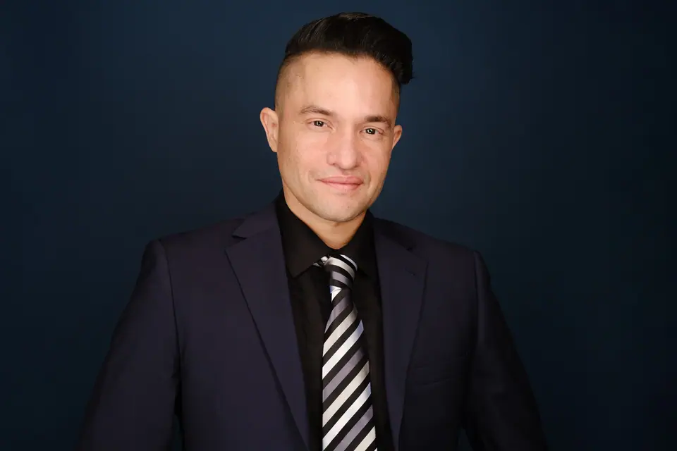 Headshot of a man in a dark suit and striped tie on a navy backdrop