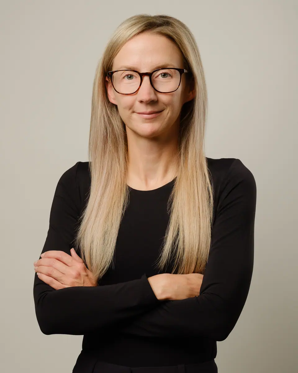 Healthcare headshot of a smiling woman with glasses and long blonde hair, arms crossed