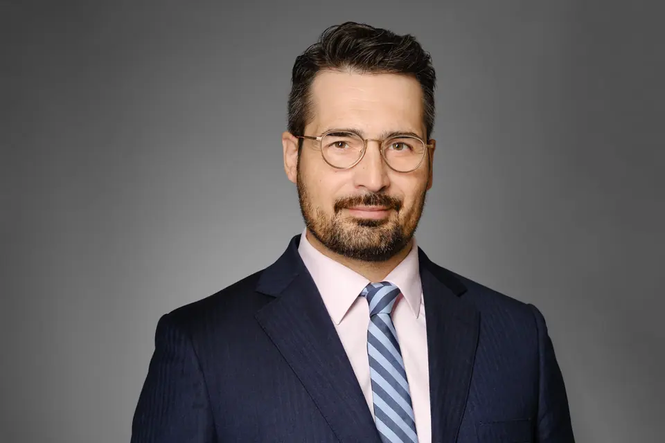 Lawyer headshot of a man with glasses in a navy suit and striped tie