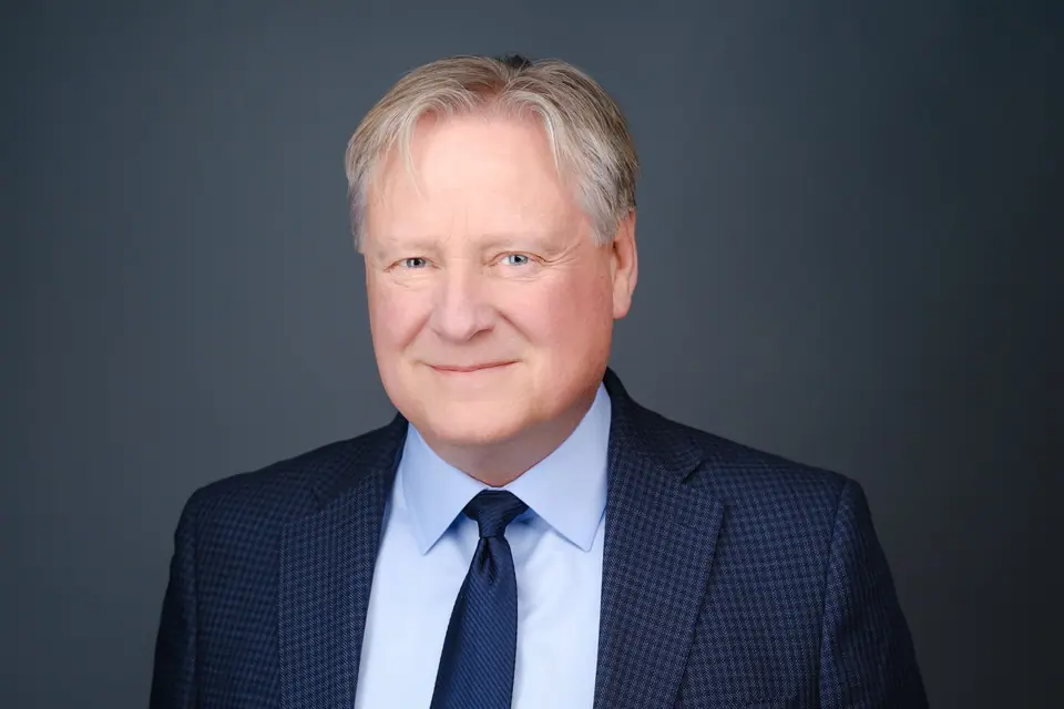 LinkedIn headshot of a smiling man with silver hair in a navy suit and tie