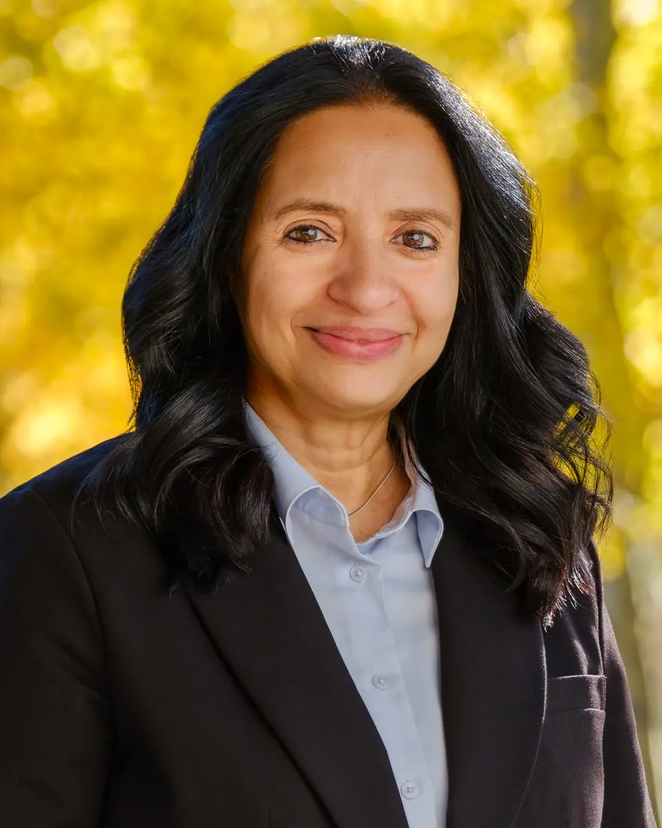 Outdoor portrait of a smiling woman in a blazer with autumn leaves behind her