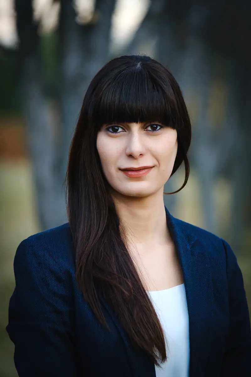 Outdoor portrait of a woman with dark hair and bangs in a navy blazer
