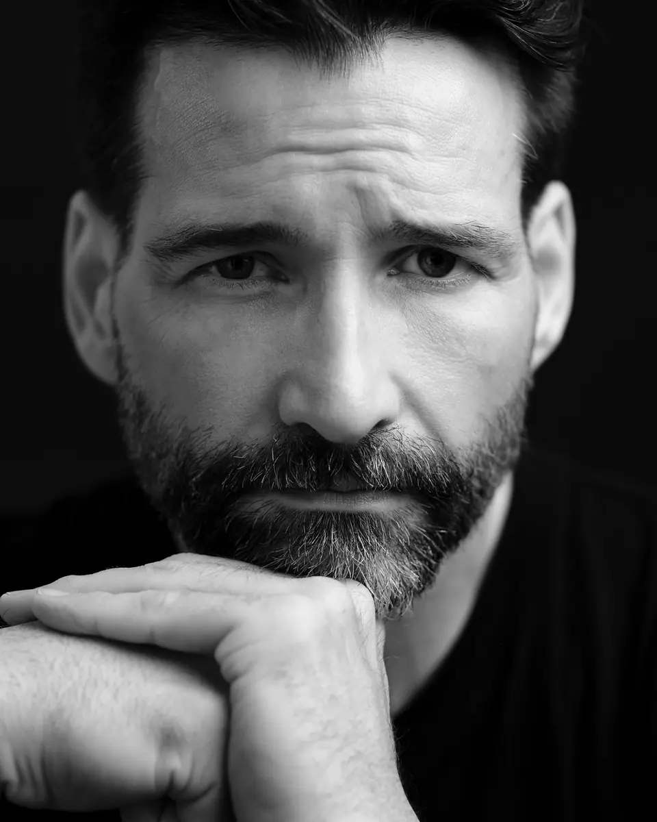 Dramatic black and white portrait of a bearded man with his hand at his chin