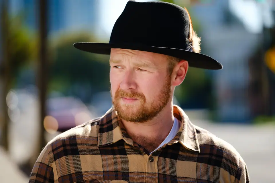 Outdoor portrait of a man with a red beard in a black hat and plaid shirt