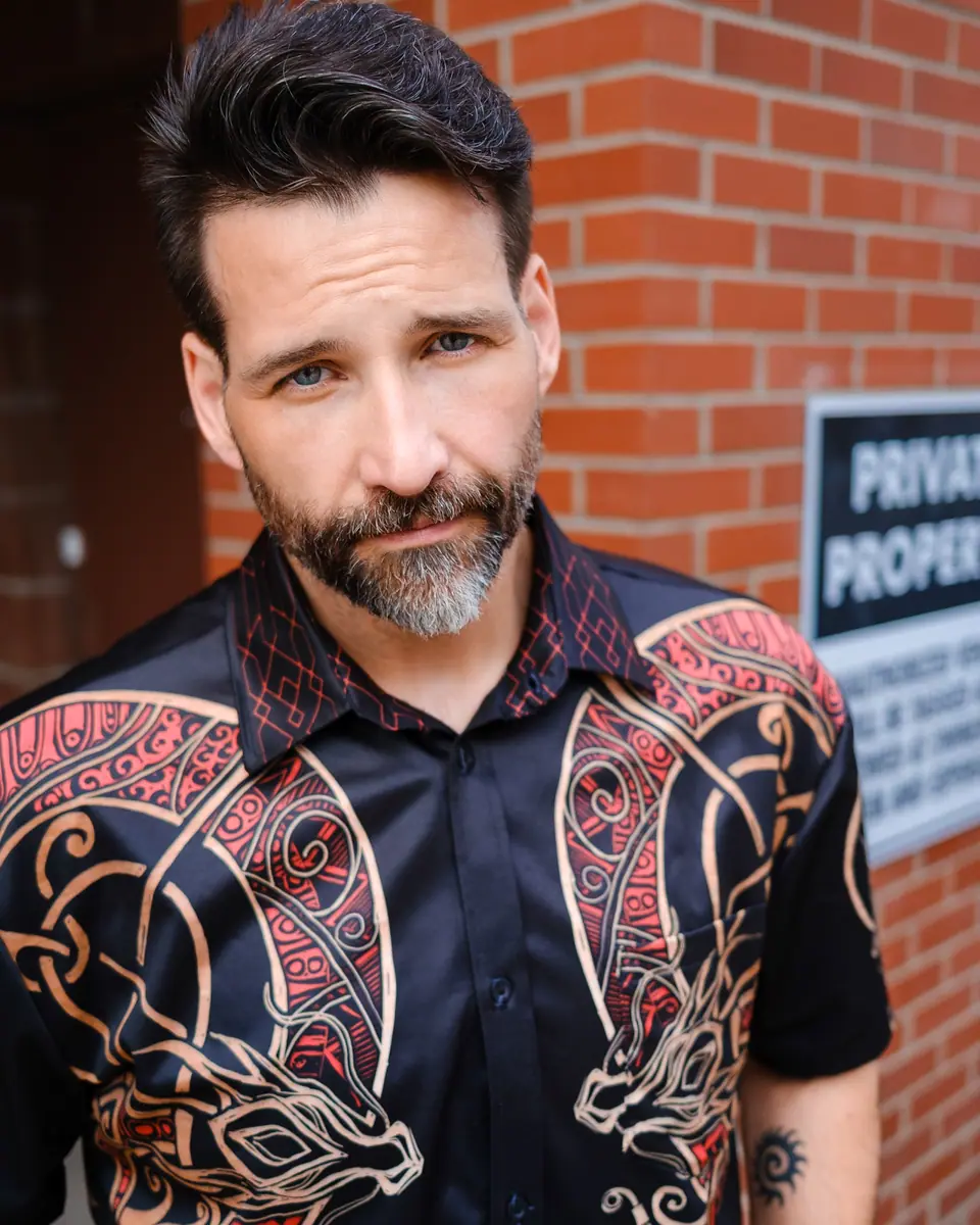 Outdoor portrait of a bearded man in a patterned shirt against red brick