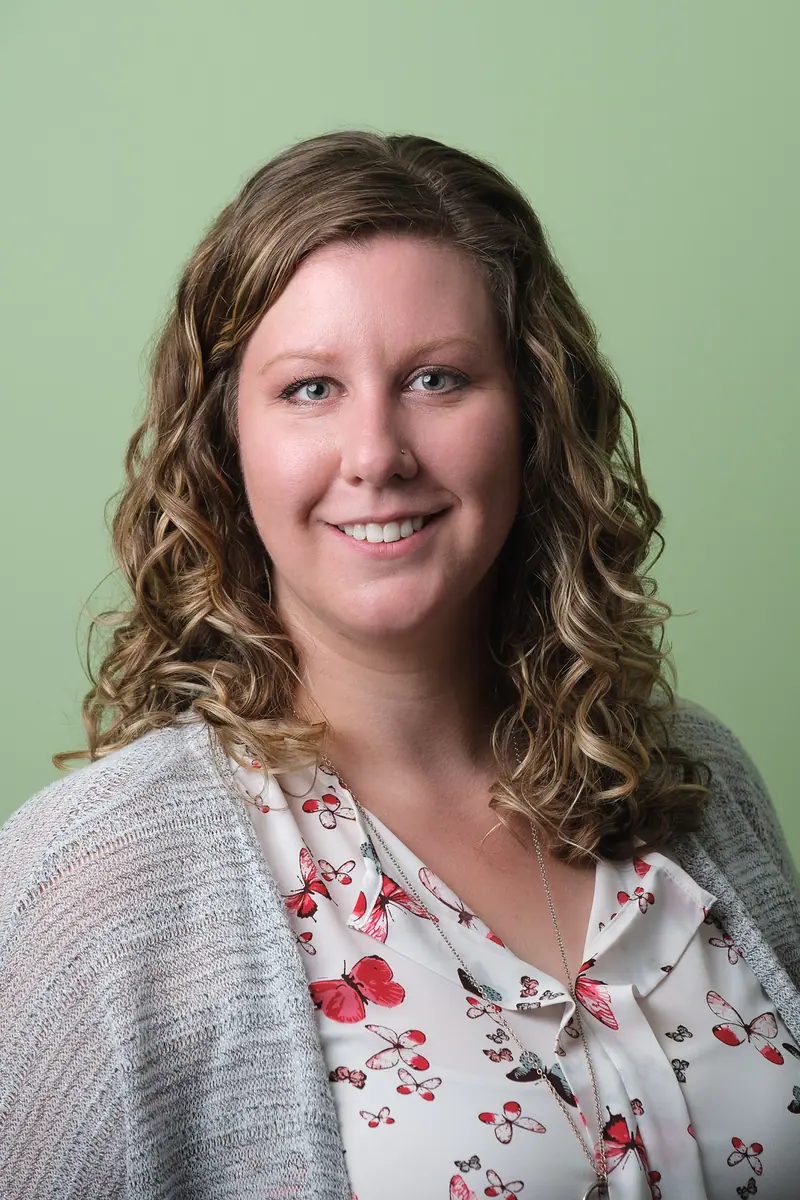 Portrait of a smiling woman with curly hair on a soft green backdrop