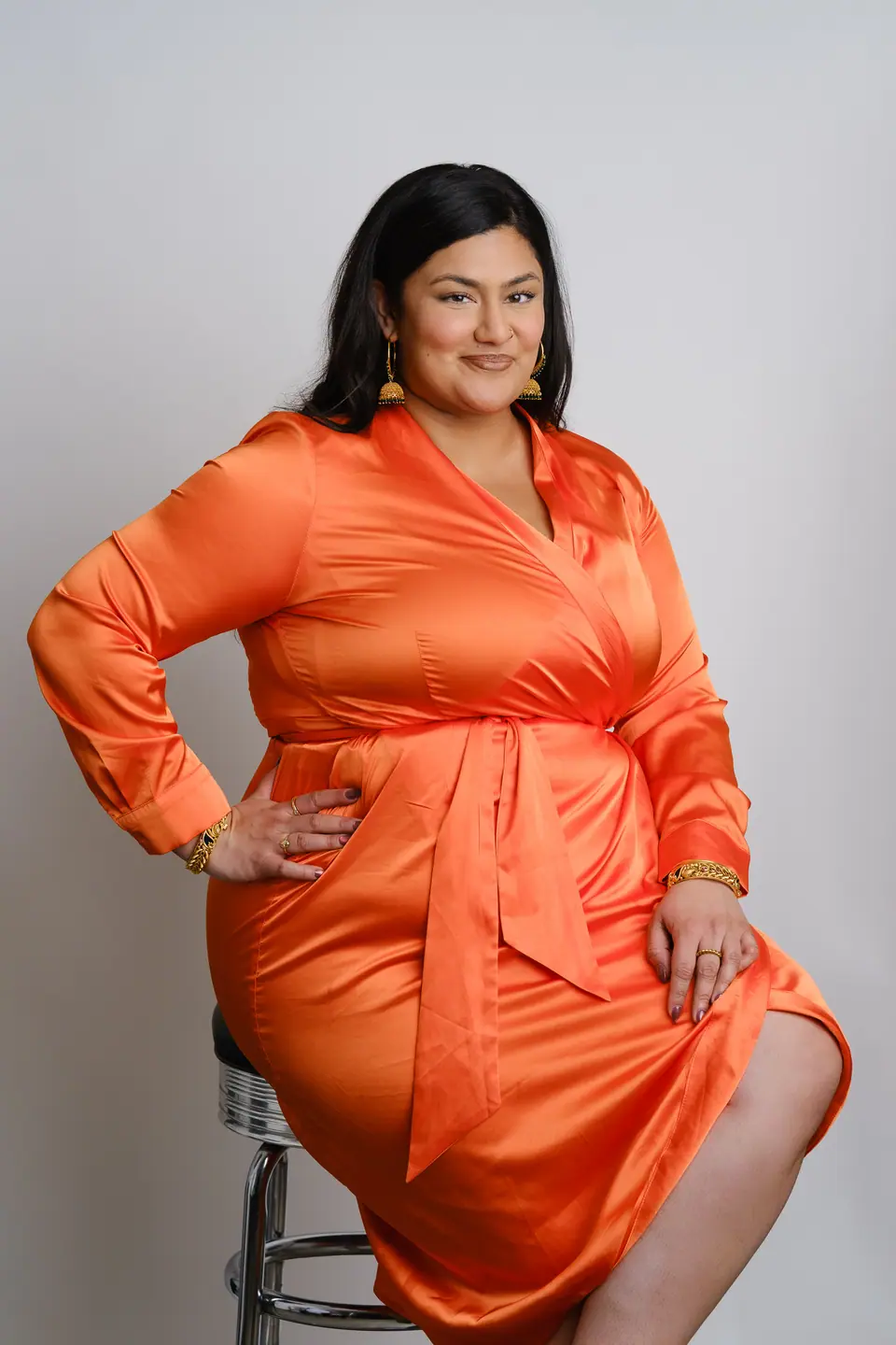 Seated studio portrait of a woman in a bright orange satin dress