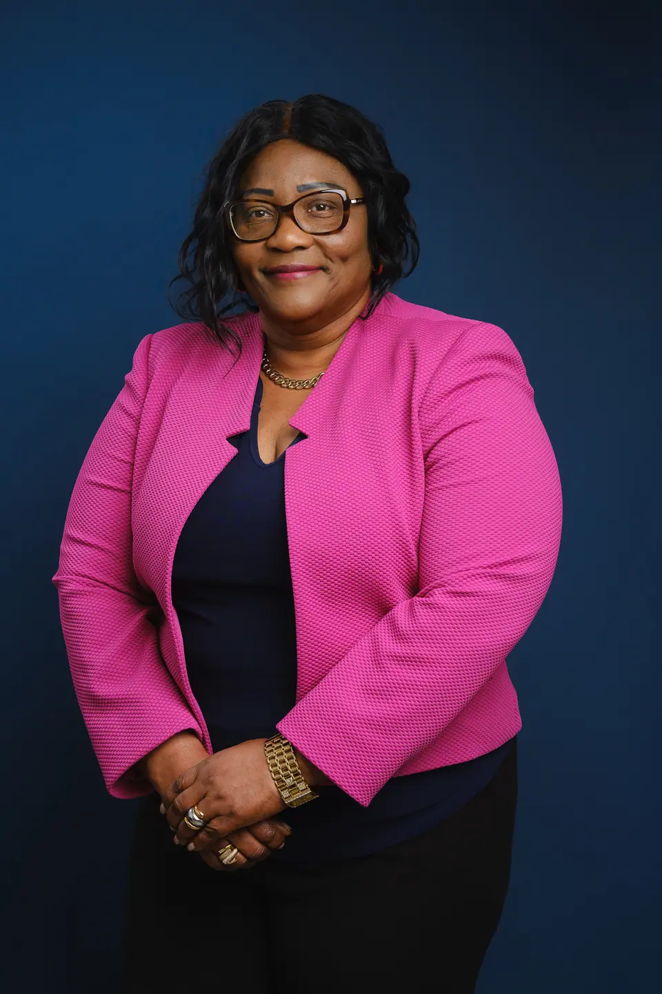 Studio portrait of a woman in a bright pink blazer on a deep blue backdrop