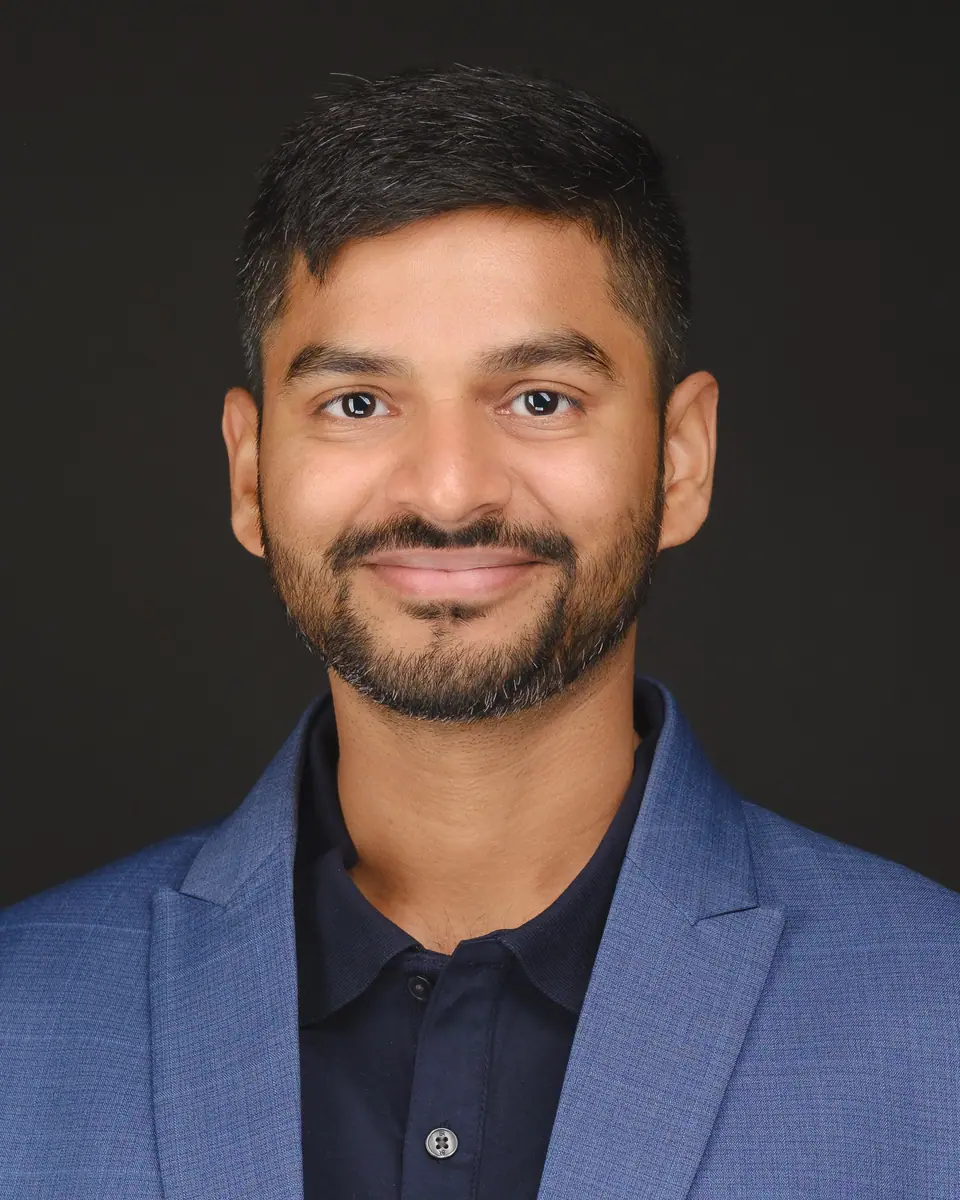 Team headshot of a smiling man with a beard in a blue blazer