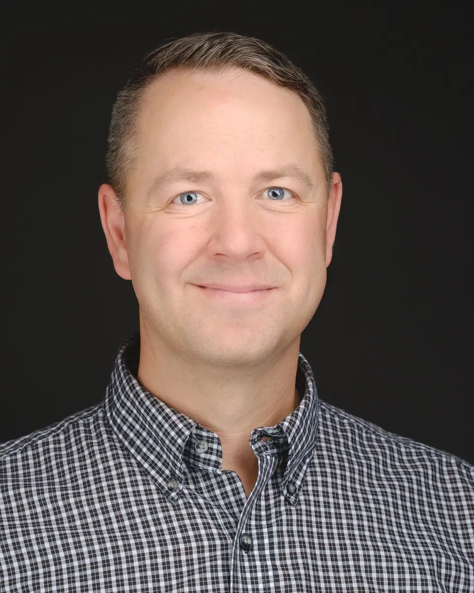 Team headshot of a smiling man in a checked shirt